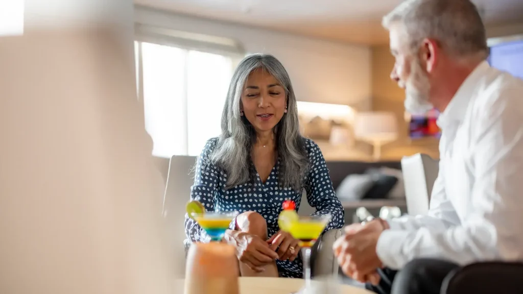 Smiling couple seated with colorful cocktails in a bright lounge.