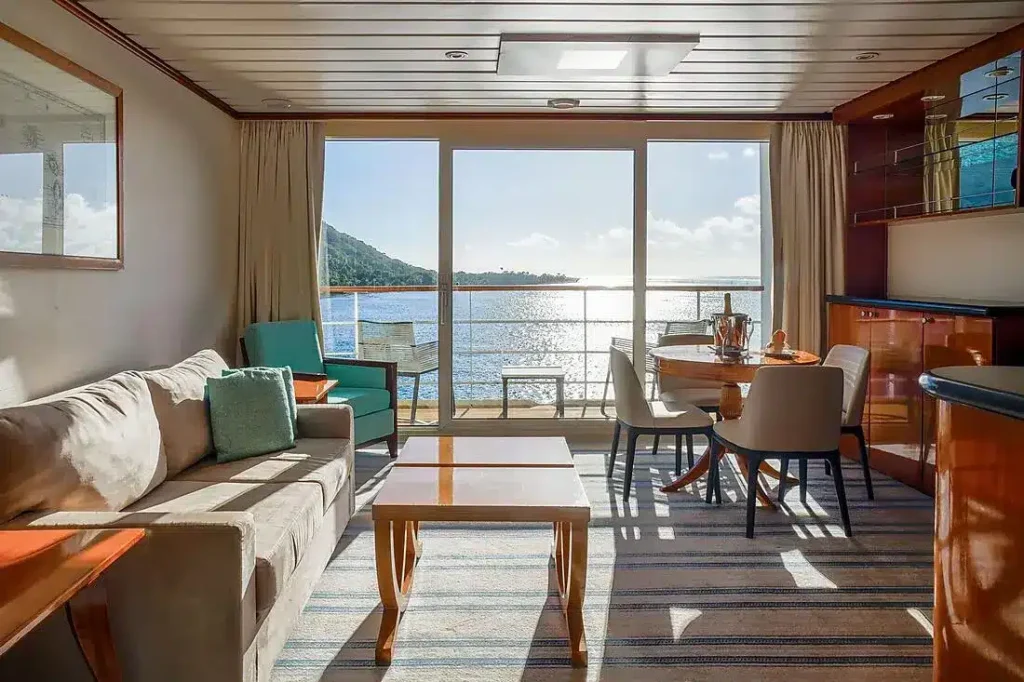 Suite living area with sofa, dining table and balcony doors opening to sea and island views.