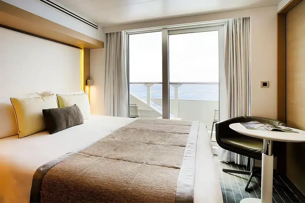 Hotel bedroom with a large bed, neutral bedding, and a balcony door opening to an ocean view.