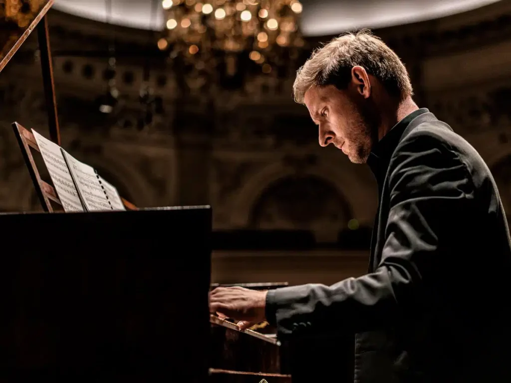 Pianist in a dark concert hall focused on sheet music at a grand piano.