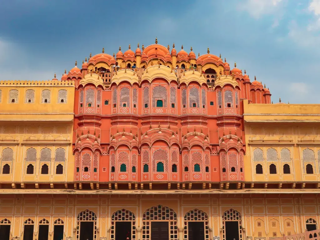 Facade of Hawa Mahal in Jaipur with pink-orange sandstone arches and many jharokhas against a blue sky