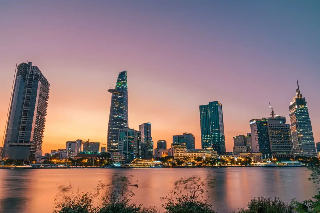 City skyline at dusk with tall skyscrapers rising along a river.