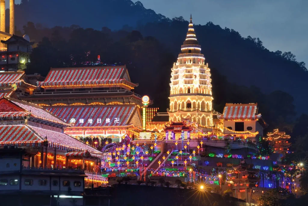 Night view of a Chinese temple complex with a tall, illuminated pagoda and festive string lights at dusk.