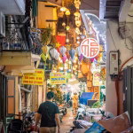 Narrow alley at night lined with paper lanterns, shopfronts and signs.