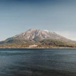 Coastal landscape with a rocky mountain island rising above calm blue waters under a clear sky