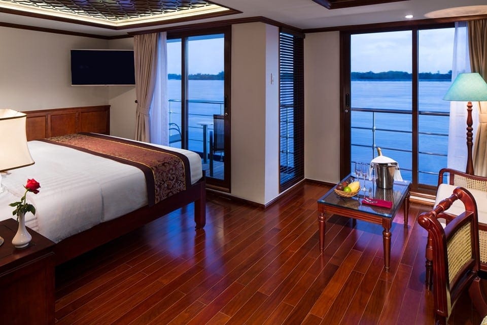 Hotel room with a king bed, wooden floor, and balcony doors opening to a water view.