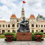Yellow colonial-style city hall with a bronze statue of a man and child in front.