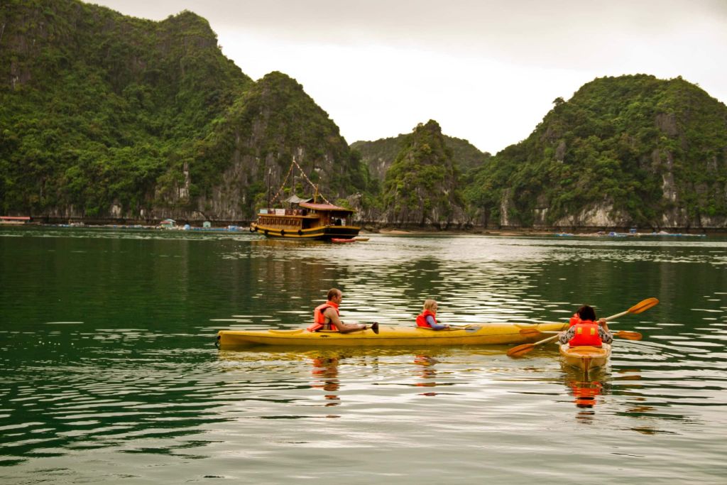 Two people in orange life vests kayaking in a yellow kayak among karst cliffs.