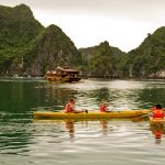 Two people in orange life vests kayaking in a yellow kayak among karst cliffs.