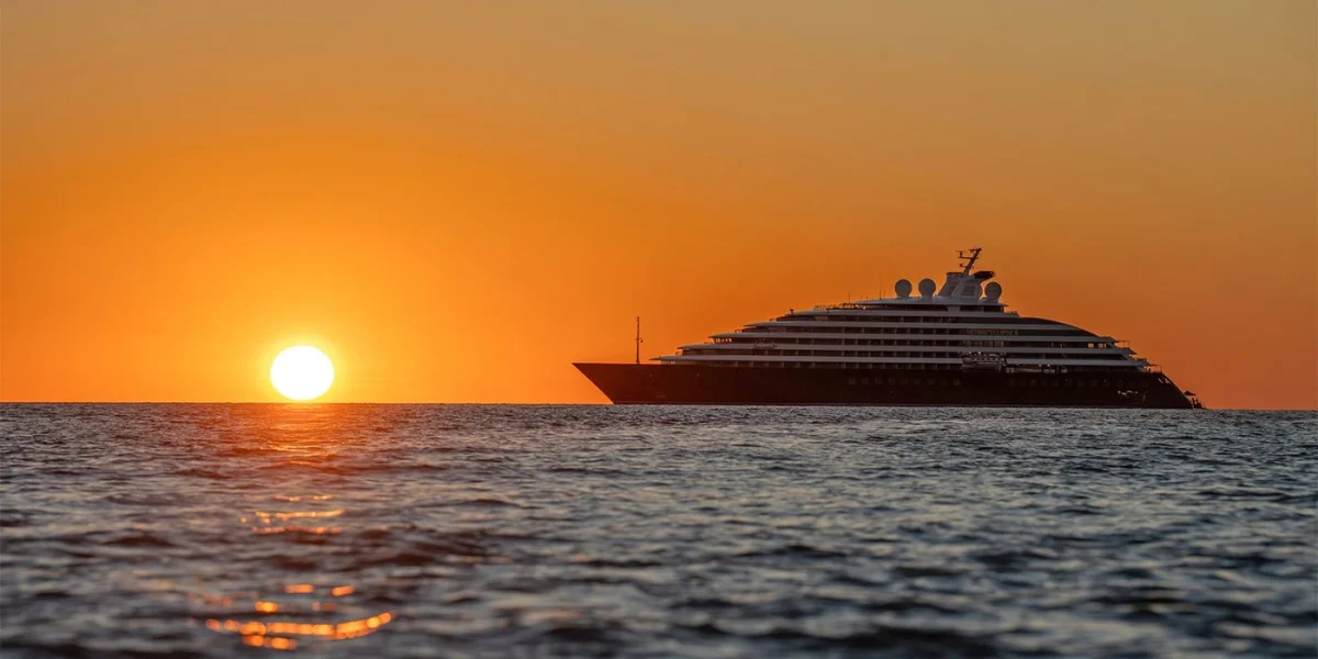 Luxurious yacht cruising on calm sea at sunset with orange sky and bright sun near the horizon