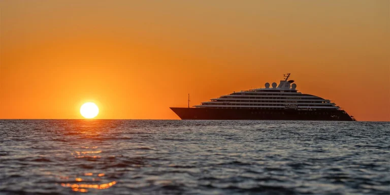 Luxurious yacht cruising on calm sea at sunset with orange sky and bright sun near the horizon