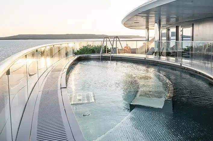 Infinity pool on the deck of a luxury yacht with glass railings and ocean view in the background.
