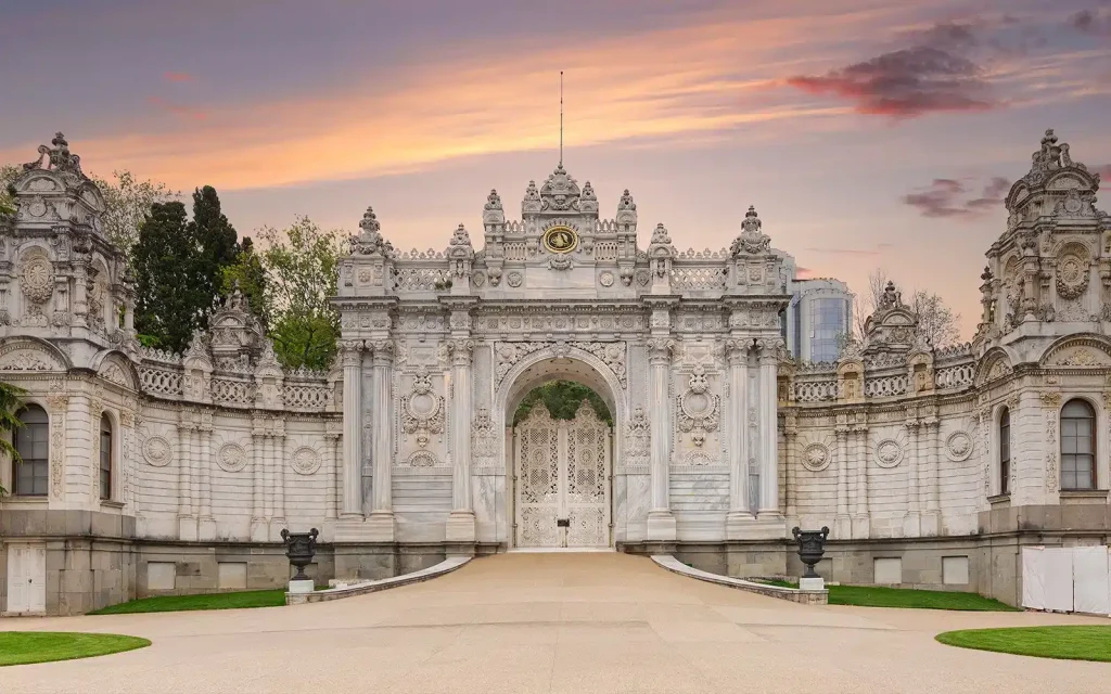 Elaborate white marble gate with intricate carvings and statues at sunset.