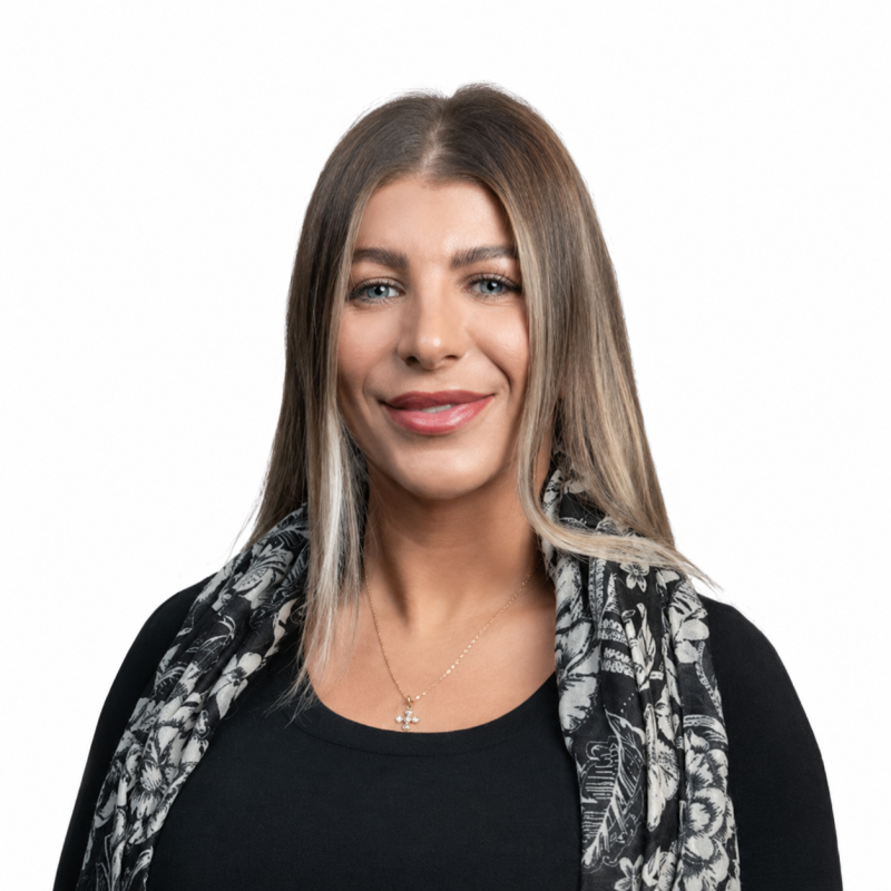 Head-and-shoulders portrait of a smiling woman with light brown hair, wearing a black top and patterned scarf, and a small pendant necklace.
