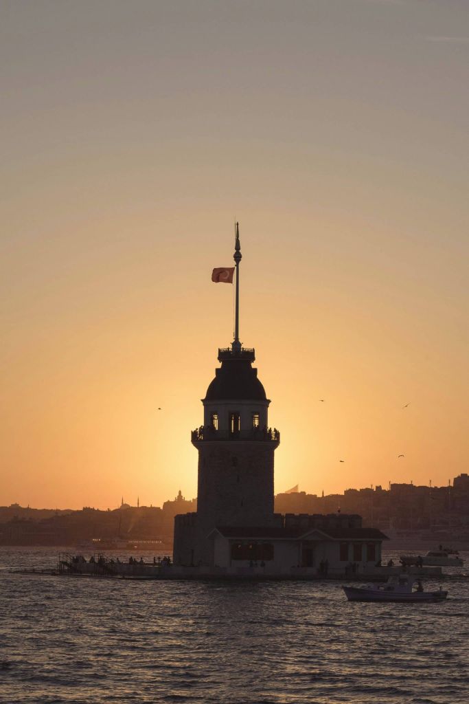 Sunset over the Maiden's Tower with a Turkish flag on top, silhouette against a orange sky over the water.