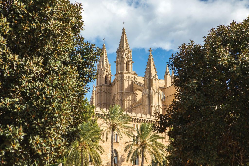 Gothic cathedral spires framed by dense green trees against a blue sky