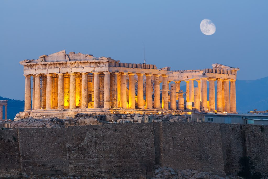 Parthenon on the Acropolis lit up at dusk with a full moon rising above.