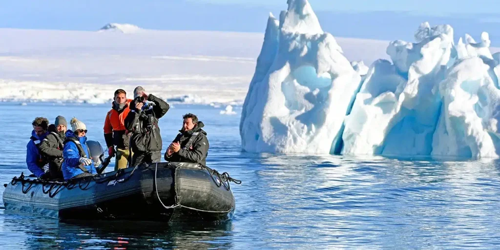 Group of people in a black inflatable boat near towering blue icebergs in icy Arctic waters, on a polar expedition route.