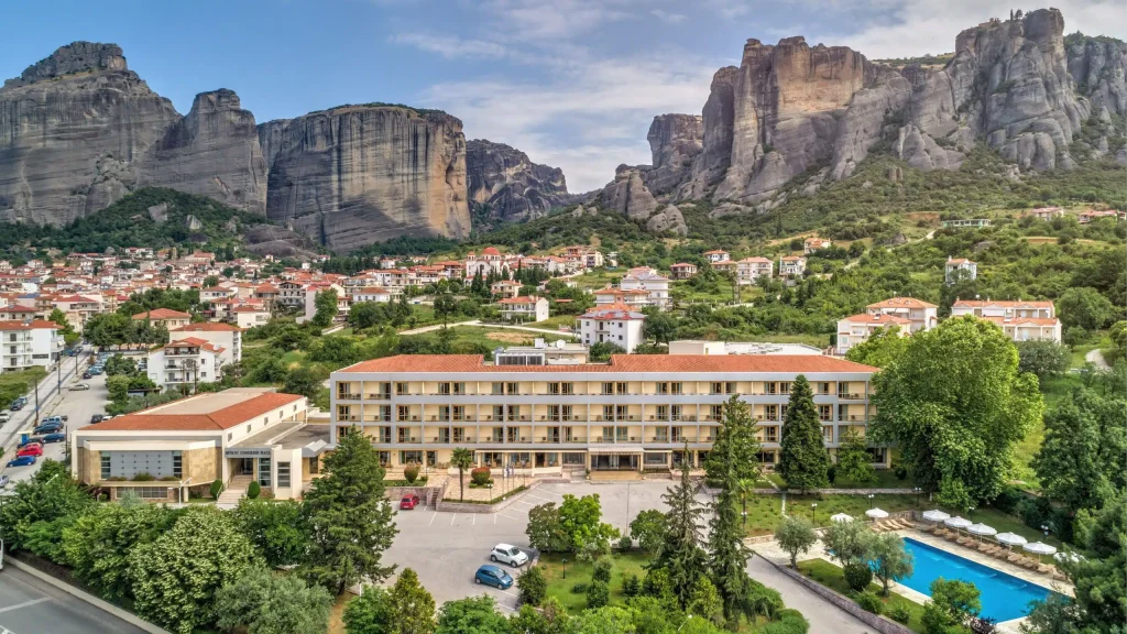Town at the base of towering rocky cliffs, with red-roofed houses and a large apartment building in the foreground.