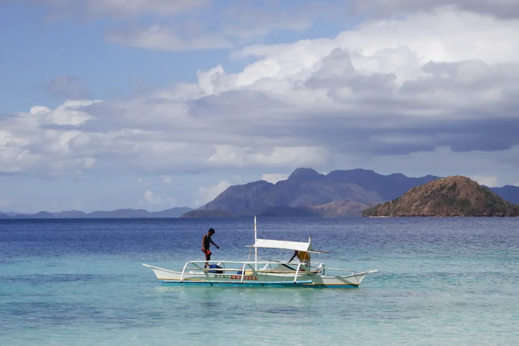 Wooden outrigger boat with a white canopy anchored in clear turquoise water beside forested islands.