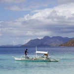 Wooden outrigger boat with a white canopy anchored in clear turquoise water beside forested islands.