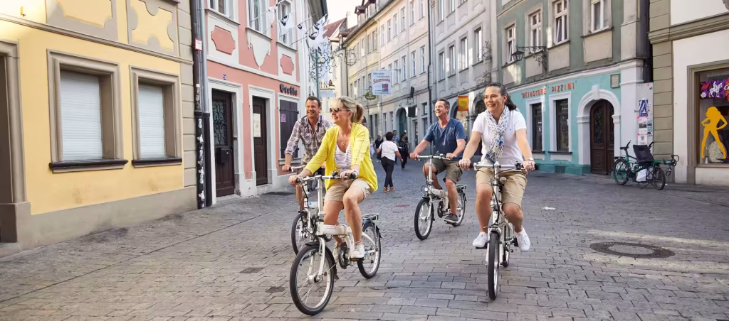 Group of four friends riding bicycles down a cobblestone street lined with colorful buildings on a sunny day.
