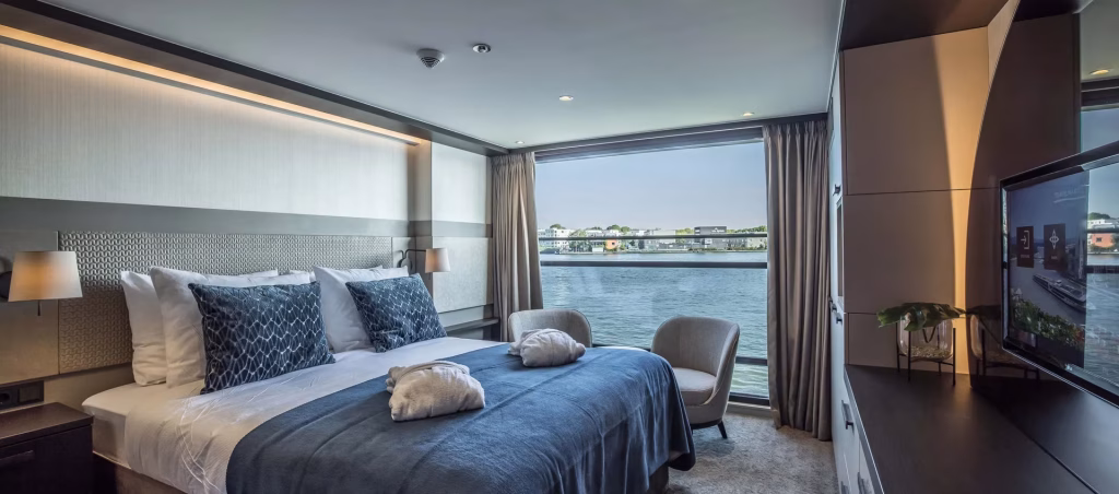 King bed with a textured headboard and blue-gray bedding, facing a large window with water view.
