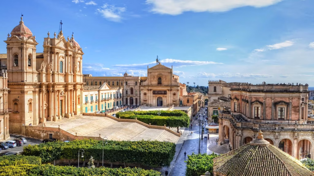 Baroque cathedral and historic stone buildings around a sunlit piazza in a hill town.