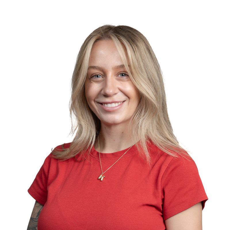Smiling woman with blonde hair wearing a red shirt, shown from shoulders up against a white background.