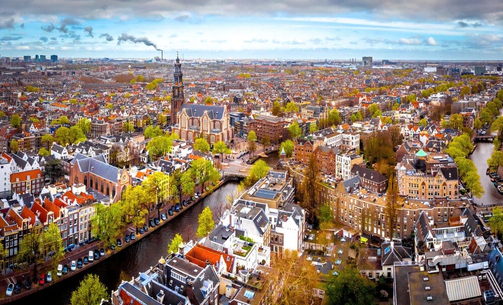 Aerial view of a European town with canals, red-tiled roofs, and a tall church spire in the center.