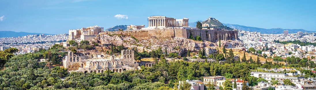 Acropolis with Parthenon atop a rocky hill in Athens, overlooking a cityscape with trees and buildings beneath a clear blue sky