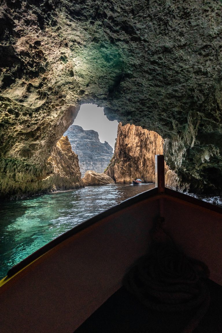Boat rides through a rugged sea cave with green water and a bright opening in the distance.