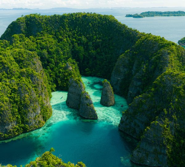 Aerial view of a tropical archipelago with green cliffs, dense forest, and turquoise water.