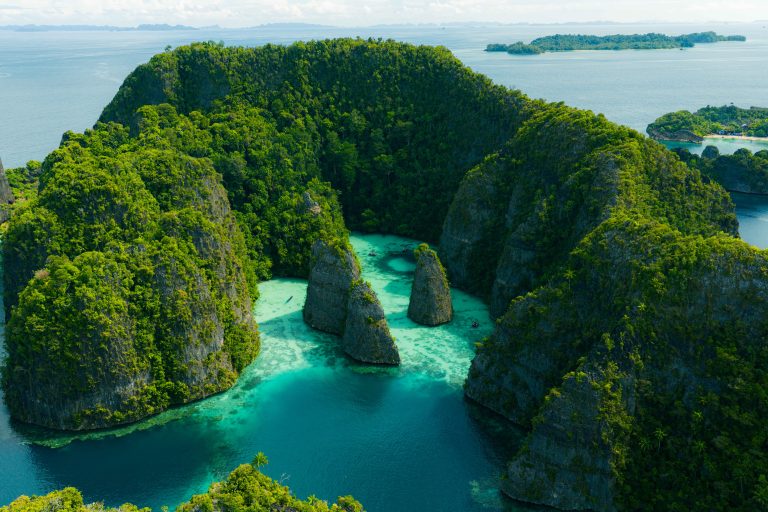 Aerial view of a tropical archipelago with green cliffs, dense forest, and turquoise water.