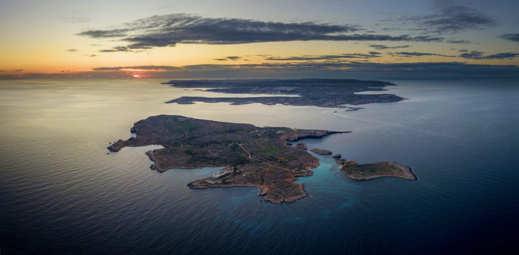 Aerial view of rocky islands at sunset with calm blue water and turquoise coves nearby.