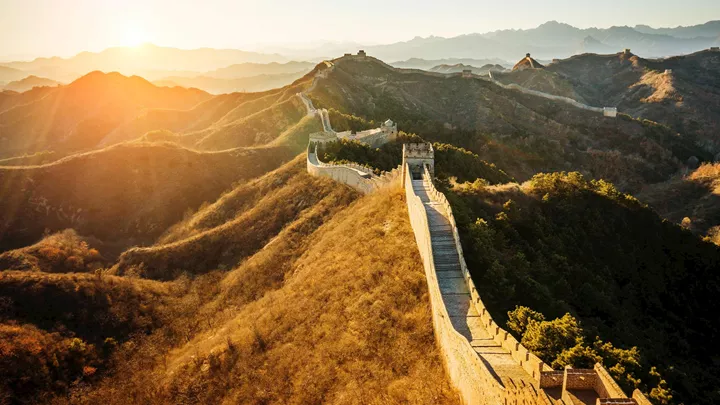 Section of the Great Wall winding over sunlit hills at sunrise, with distant watchtowers along the ridge.