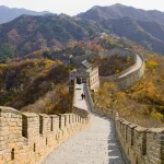 Section of the Great Wall winding through autumn-colored hills, stone steps leading toward watchtowers.