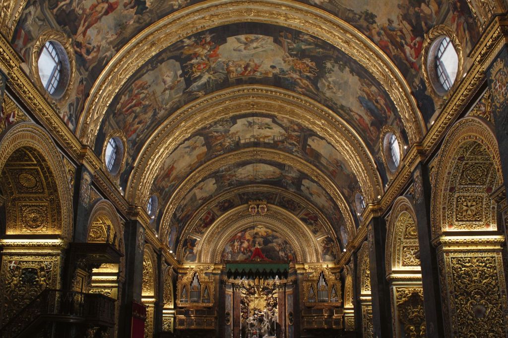 Interior of a richly gilded church with repeating gold arches and painted vaults in the nave.