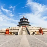 View of the Temple of Heaven’s circular, three-tiered pagoda framed by open red gates, under a blue sky.