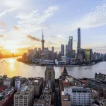 Shanghai skyline at sunset along the Huangpu River, with the Bund in the foreground and the Lujiazui towers across the water, including the Oriental Pearl Tower.