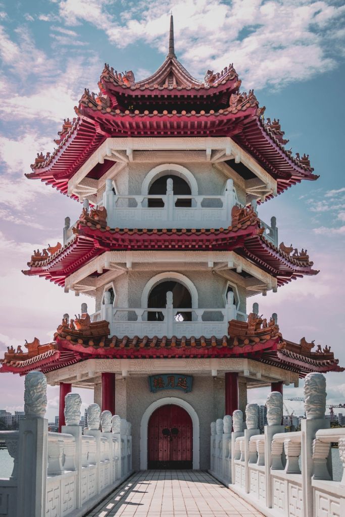 Three-tier Chinese pagoda with red tiered roofs and white stone walls under a blue sky.