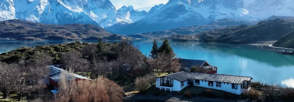 Lakeside houses and red-roofed buildings below snow-capped Patagonian peaks above a turquoise lake.