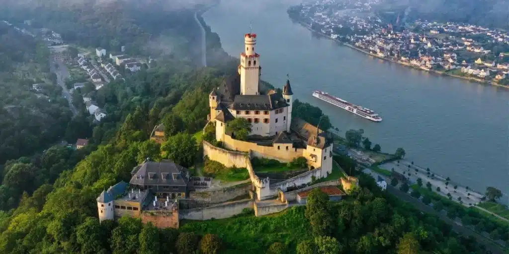 Hilltop castle above a misty river with a river cruise ship passing below.