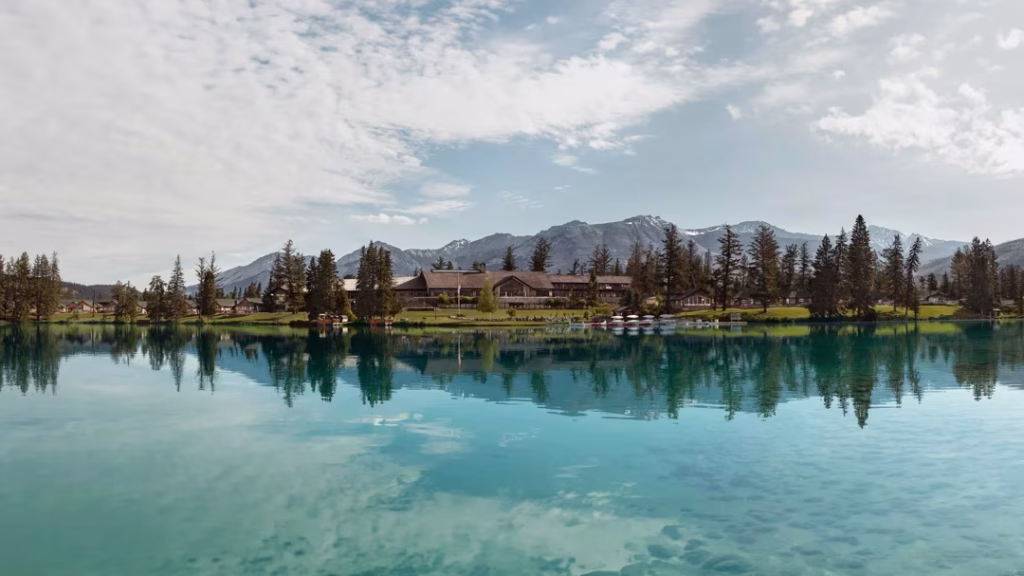 Turquoise lake with a lakeside village, pine trees, and snow-capped mountains in the distance to the horizon.