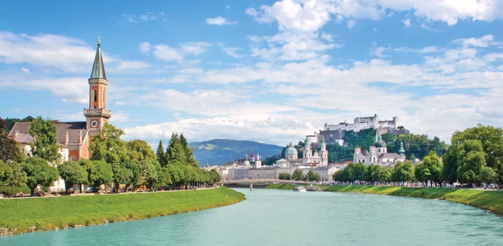 Salzburg skyline with the Salzach River, a church on the left, and Hohensalzburg Fortress atop the hill.