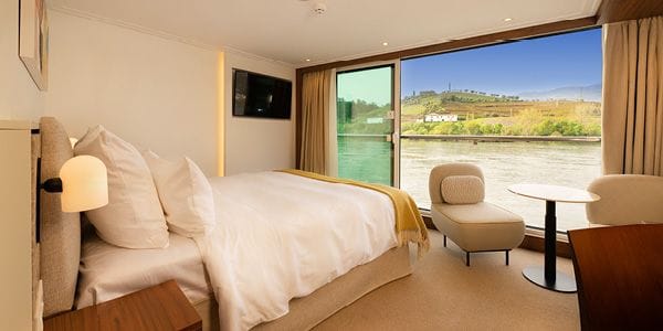 Hotel room with a king bed, white linens and a mustard throw, plus a wall-mounted TV and nightstand.